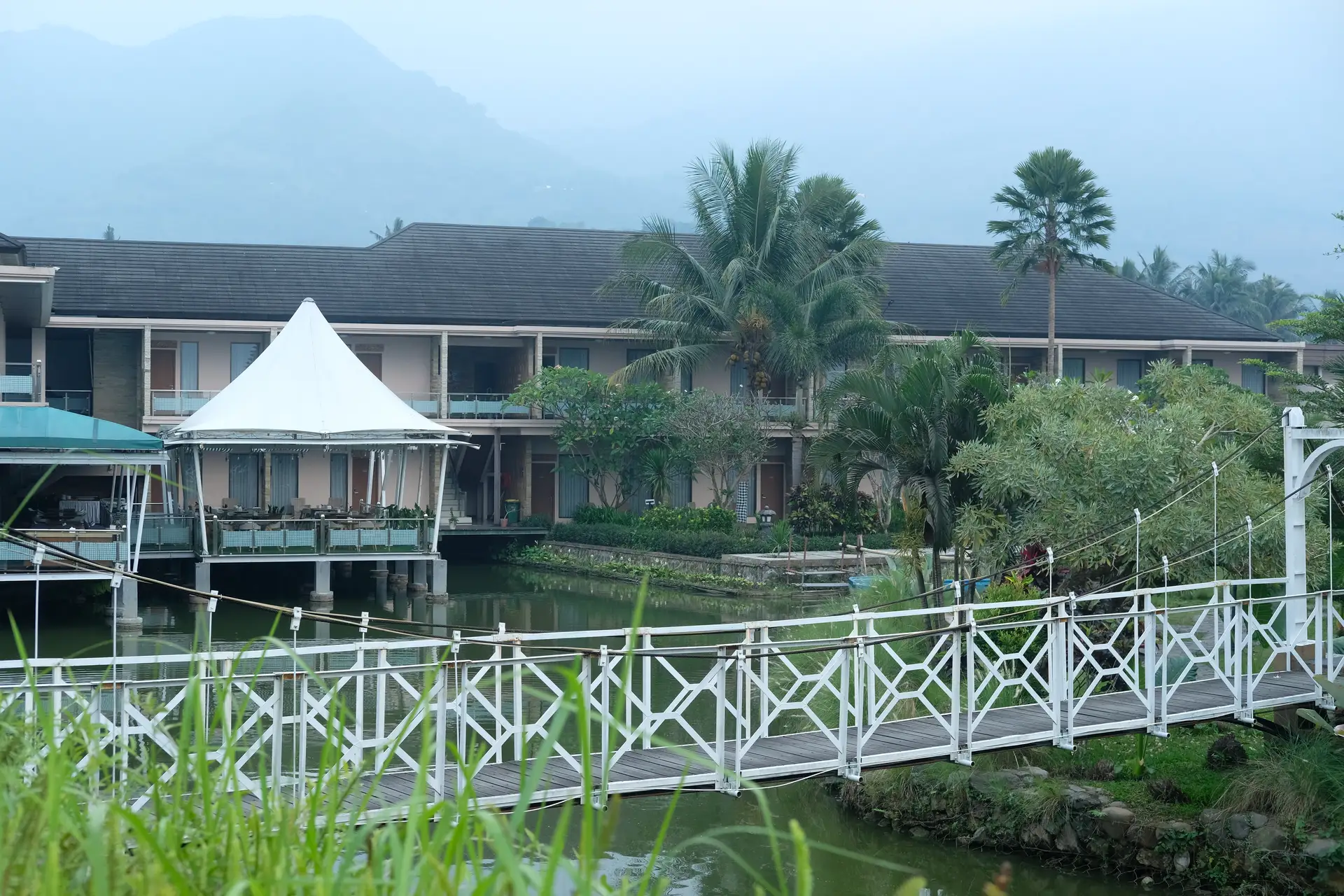 Bangunan resort, jembatan, dan kolam Rancabango berlatar gunung berkabut